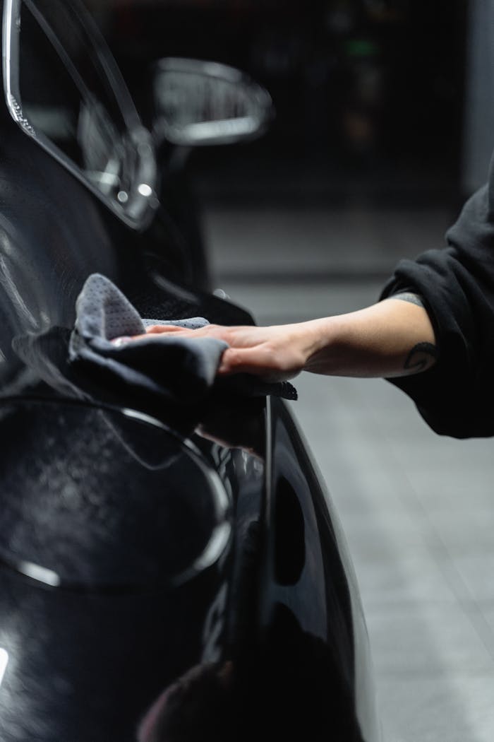 Services-03 Close-up of a persons hand cleaning a shiny black car with a microfiber cloth in a garage.