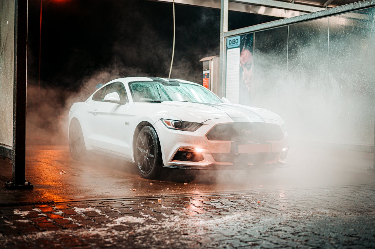 Services-01 White Ford Mustang in a misty carwash setting, illuminated at night in an urban environment.
