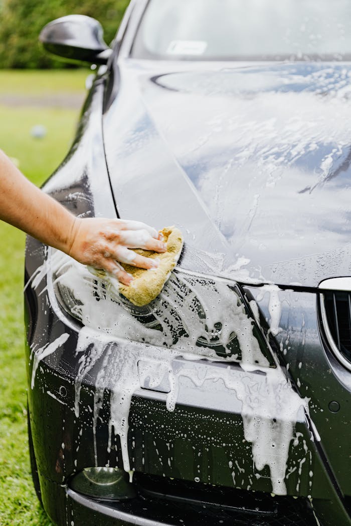 Services-02 Person washing a black cars headlight with a sponge and soap outdoors.